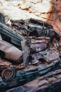 A vertical shot of rusty, stacked cars in an outdoor junkyard, surrounded by rocky desert terrain.